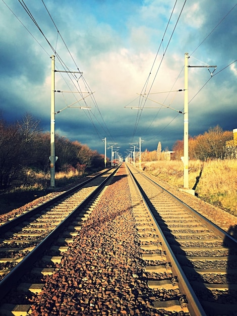 Railroad tracks against cloudy sky on sunny day