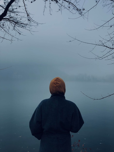 rear view of a girl standing by the lake in a foggy day