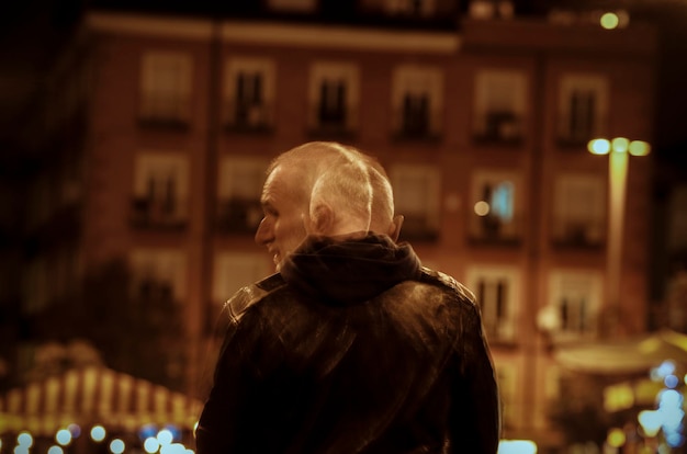 Rear view of adult man with hood on street at night