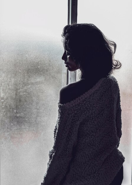 Rear view of woman standing by window at home