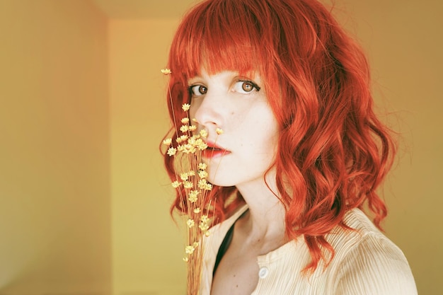Redhead woman with flowers against yellow wall