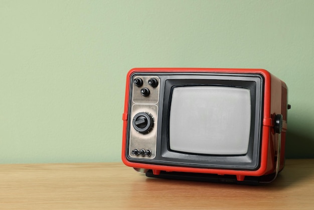 Retro tv set on wooden shelf against green wall Space for text