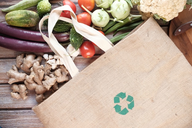 Reusable shopping bag with recycled arrows sign and vegetables on table