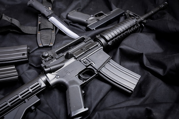 Rifle, gun, knife with sheath, compass and notebook with pen on on black cloth