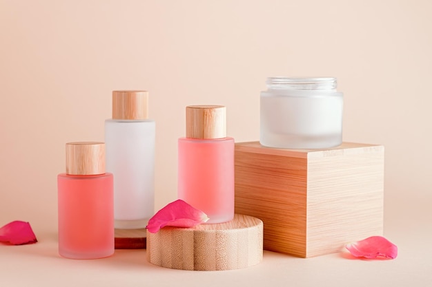 Rose extract natural cosmetics in reusable bottles and rose petals on wooden risers Plant based organic cosmetics still life