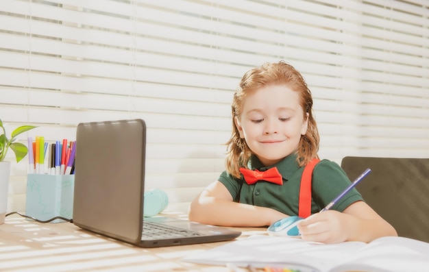 schoolboy studying and using computer laptop and writing on notebook nerd pupil