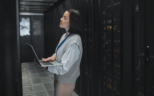 Server room laptop and young woman or technician in data center management system and cyber security Thinking serious and inspection of asian electrician engineer or programmer person code check