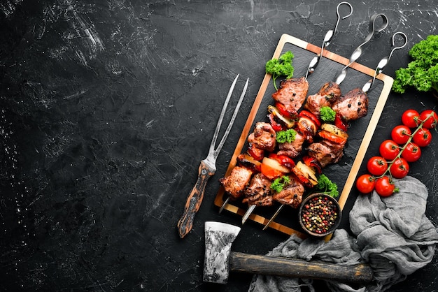 Shish kebab BBQ meat with onions and tomatoes On a black background Top view Free space for your text Rustic style