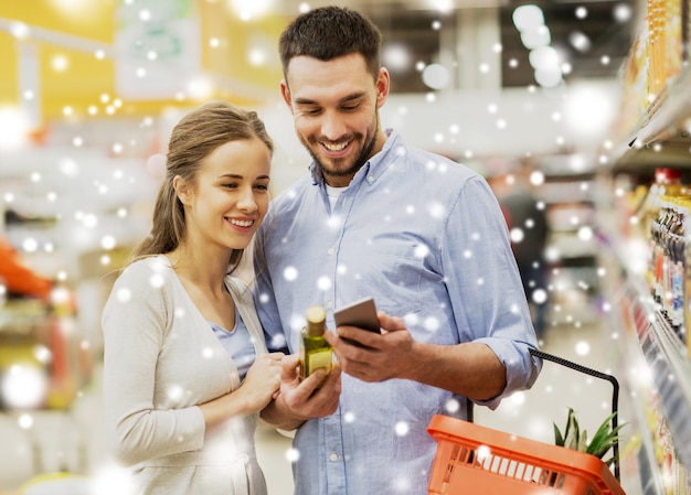shopping food sale consumerism and people concept happy couple with smartphone buying olive oil at grocery store or supermarket over snow