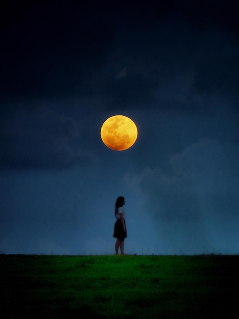 Side view of young woman standing on field against full moon in sky
