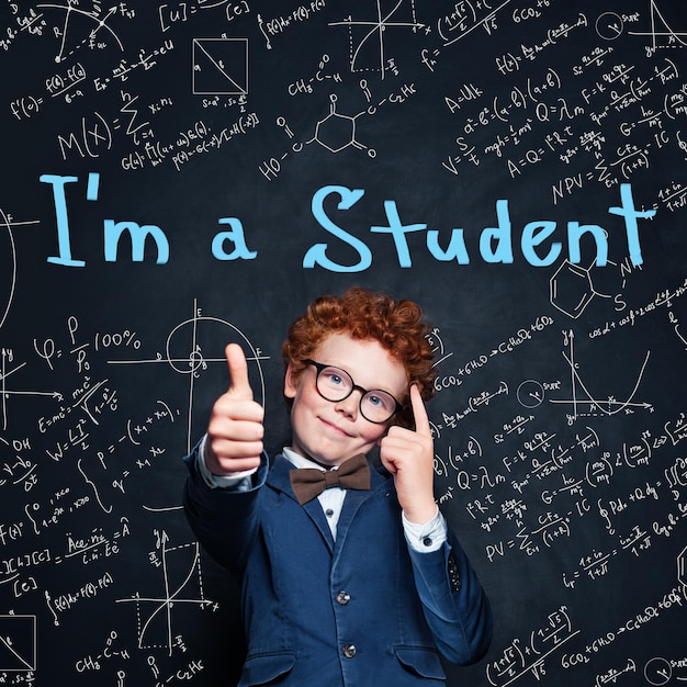 Smart child schoolboy showing thumb up on blackboard background Back to school concept