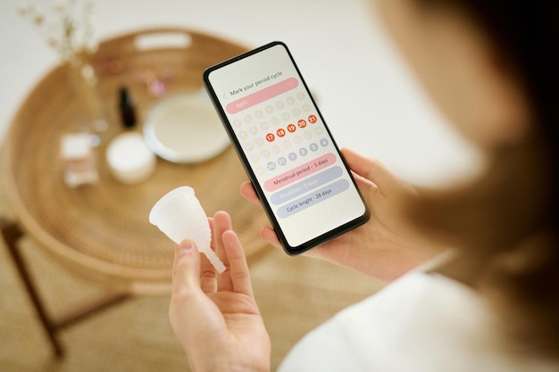 smartphone and menstrual cup in female hands