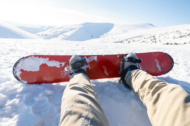 Foto snowboarder sitting on relax moment at sunset in french alps ski resort - winter sport concept with person on top of the mountain ready to ride down - legs view point with warm backlighting filter