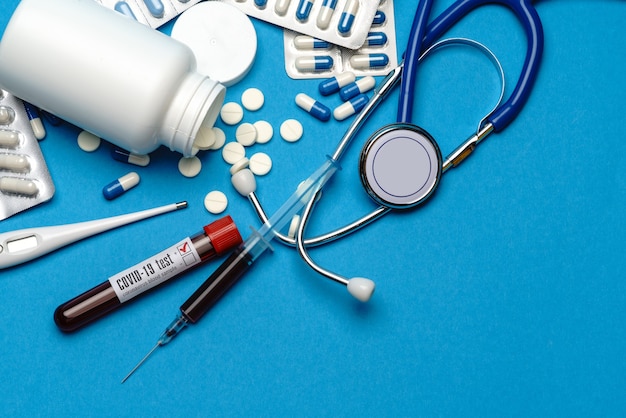 Stethoscope, syringe, thermometer, blood test tube and can of pills on blue background top view with