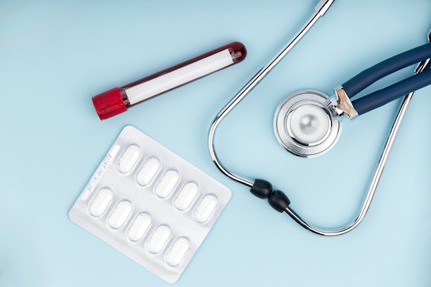 Stethoscope with pills and tube of blood test on blue background.