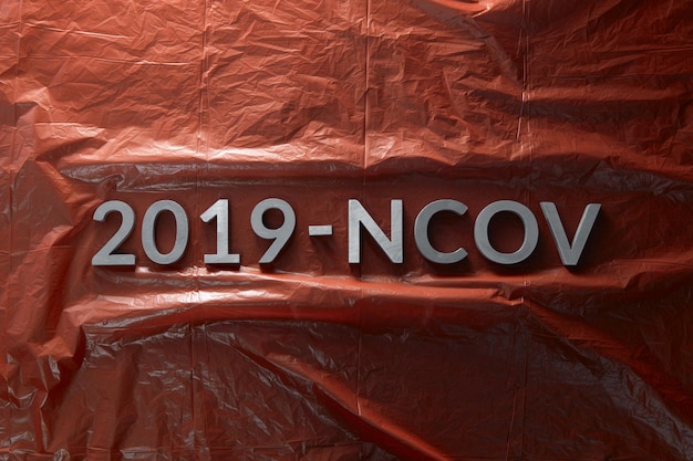 The word 2019NCOV laid with metal letters on crumpled red plastic film background in flat lay composition