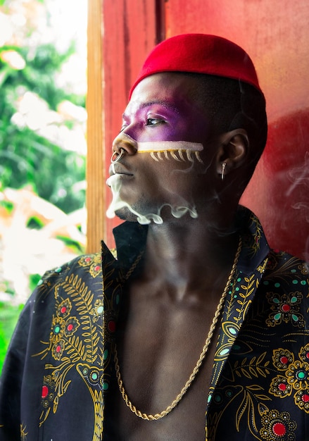 Thoughtful man with face paint emitting smoke against wall