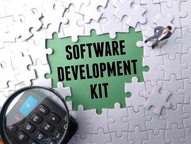 Toppvisning av kalkulator, forstørrelsesglass og miniatyrfolk med teksten "SOFTWARE DEVELOPMENT KIT" på en hvit puslespillbakgrunn