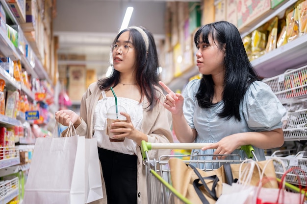 Two young Asian women shop together in a grocery store focused on selecting items from the shelves