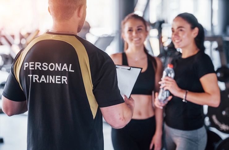 Foto two young girls in sportive clothes is in the gym together at daytime with their male personal trainer.