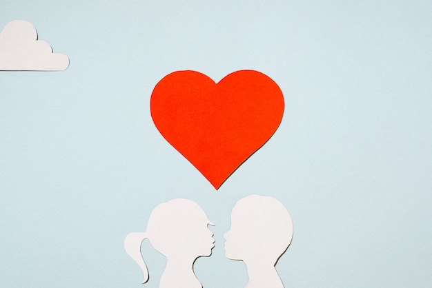 Valentine's Day concept. Kissing girl and boy silhouettes. Creative love card. Red heart and clouds on a pastel blue background. Flat lay, top view.