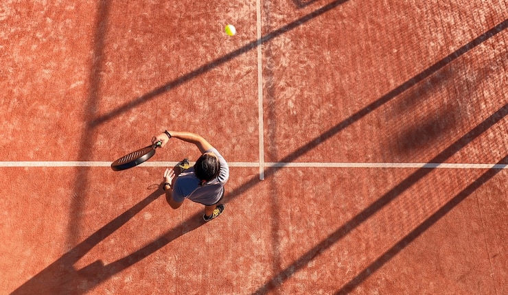 Foto view from above of a paddle tennis player hitting the ball with the racket on an outdoor court.