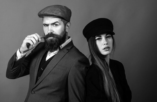 Vintage retro couple on red wall old style hat on bearded man and black fashion cap on beauty woman