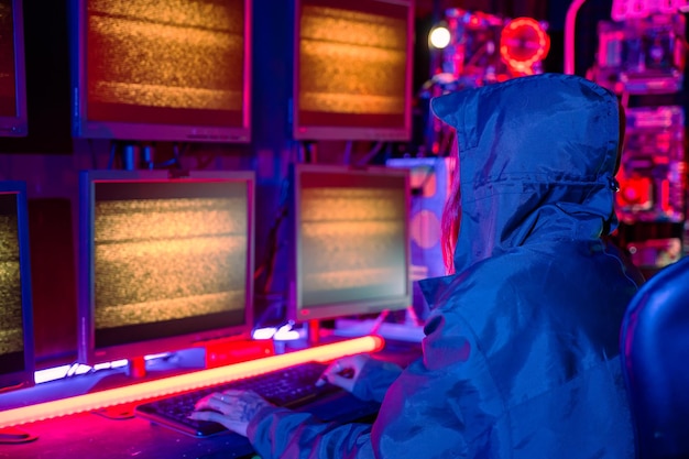 Woman hacker wear hood sit front computer typing on keyboard hacking servers in neon light gamer