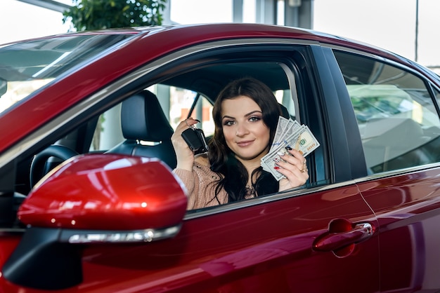 Woman sitting in new car and showing dollars and keys