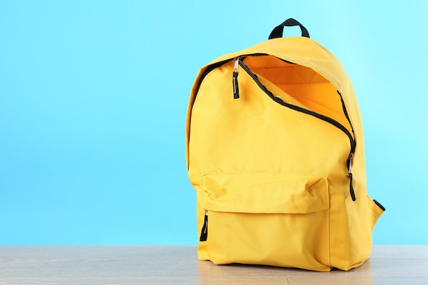 yellow backpack on wooden table against light blue background space for text