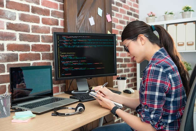young female programmer working in office and writting something down on her note.