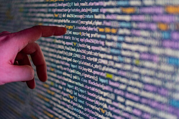 A closeup image of a persons hand pointing at a code display on a large screen likely in a modern software development workspace or educational setting The hand is wearing a watch