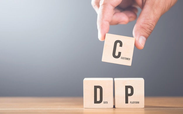 A hand arranging wooden blocks with the letters C D and P on a table Represents the concept of building a customer data platform emphasizing the importance of integrating these elements