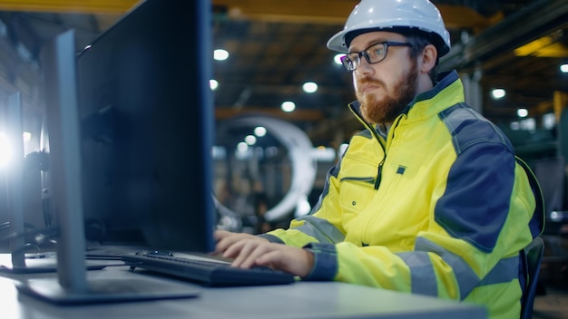 A man in a yellow jacket is typing on a computer.