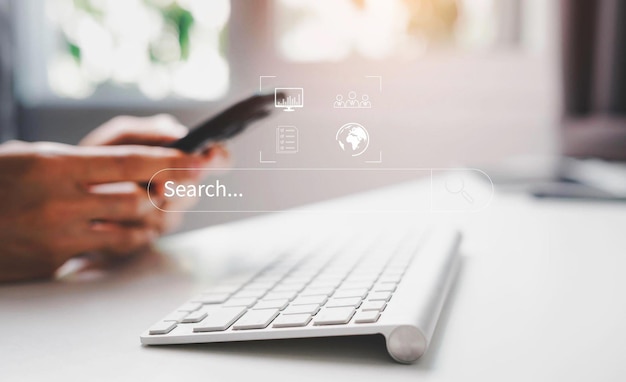A person holding a phone in front of a keyboard with a screen that says search...