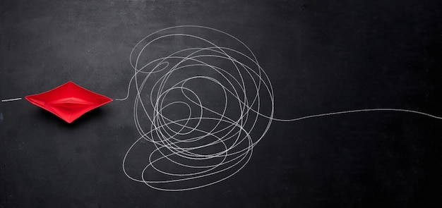 A red paper boat and a tangled trajectory drawn in chalk The concept of difficult decisions a long way and overcoming difficulties