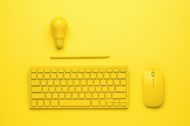 A yellow keyboard with a mouse, a pencil and a light bulb on a yellow background. Monochrome.
