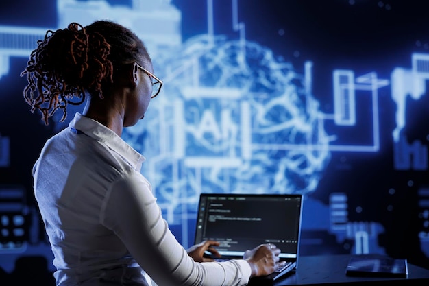 African american engineer updating AI systems, writing intricate binary code scripts on laptop. Tech support using programming to upgrade artificial intelligence simulation model