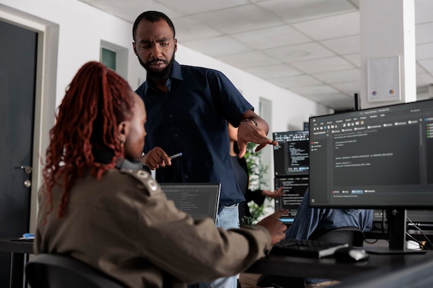African american engineers typing machine learning html code on computer, sitting at desk table in big data office. Software developers working on database system with html script in it security agenc