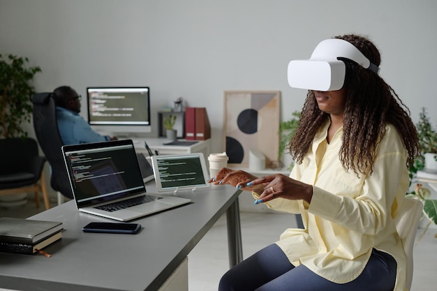 African american office worker with vr headset sitting at table and imitating typing on invisible