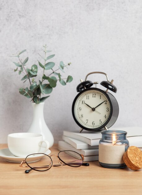 Alarm clock books coffee cup eyeglasses and candle creating cozy atmosphere on wooden desk