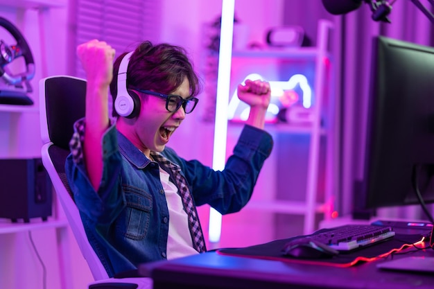 asian attractive esport male gamer play online video game on computer handsome man gaming player feel happy and excited enjoy technology broadcast live streaming while plays cyber tournament at home