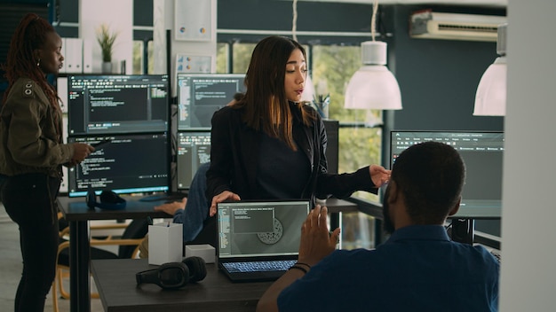 Asian database programer explaining software development with server code, using laptop to show terminal window to coder. App developer typing big data for firewall security in agency office.