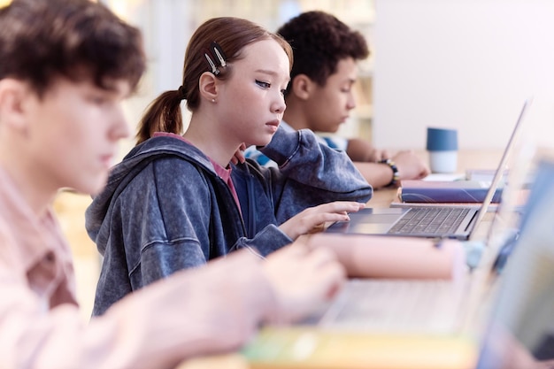 Asian girl using computer in school in row with group of students