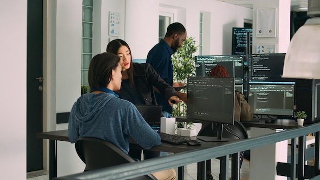 Asian team of artificial intelligence cloud programers talking about programming in it agency office. Compiling code on terminal window server, doing teamwork on developing algorithms.