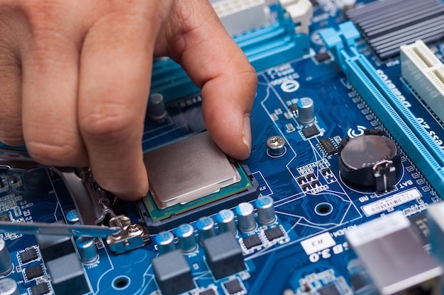 Assembling high performance personal computer, inserting CPU, processor into the motherboard socket, opened PC case in background, shallow depth of field, focus on hand