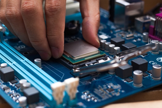 Assembling high performance personal computer, inserting CPU, processor into the motherboard socket, opened PC case in background, shallow depth of field, focus on hand