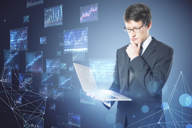 Attractive young european businessman using laptop with creative forex charts on blurry background Trade and economy concept Double exposure