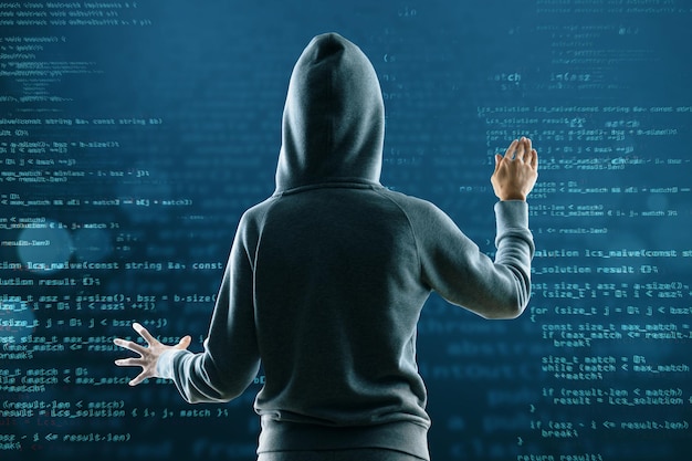 Back view of hacker in hoodie on abstract coding background Hacking and technology concept