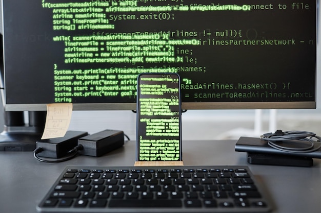 Background image of computer screen with green code lines focus on smartphone in foreground copy spa